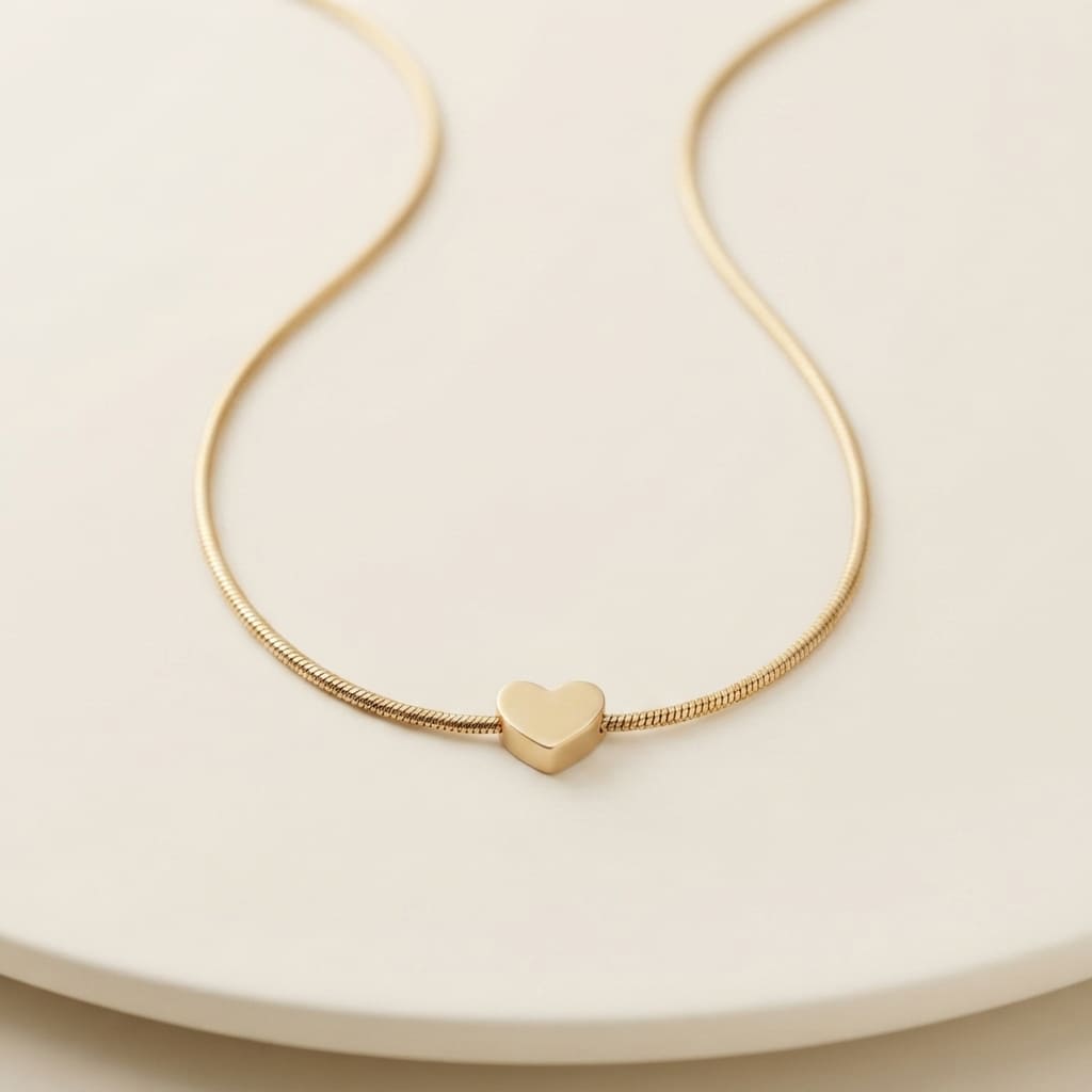 Delicate gold snake chain necklace with a small polished heart pendant displayed on a smooth cream surface - Snap Mart Pakistan
