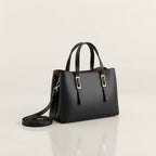 A black leather tote bag with double top handles, a detachable shoulder strap, and gold-tone metal accents, displayed on a clean light beige studio background.