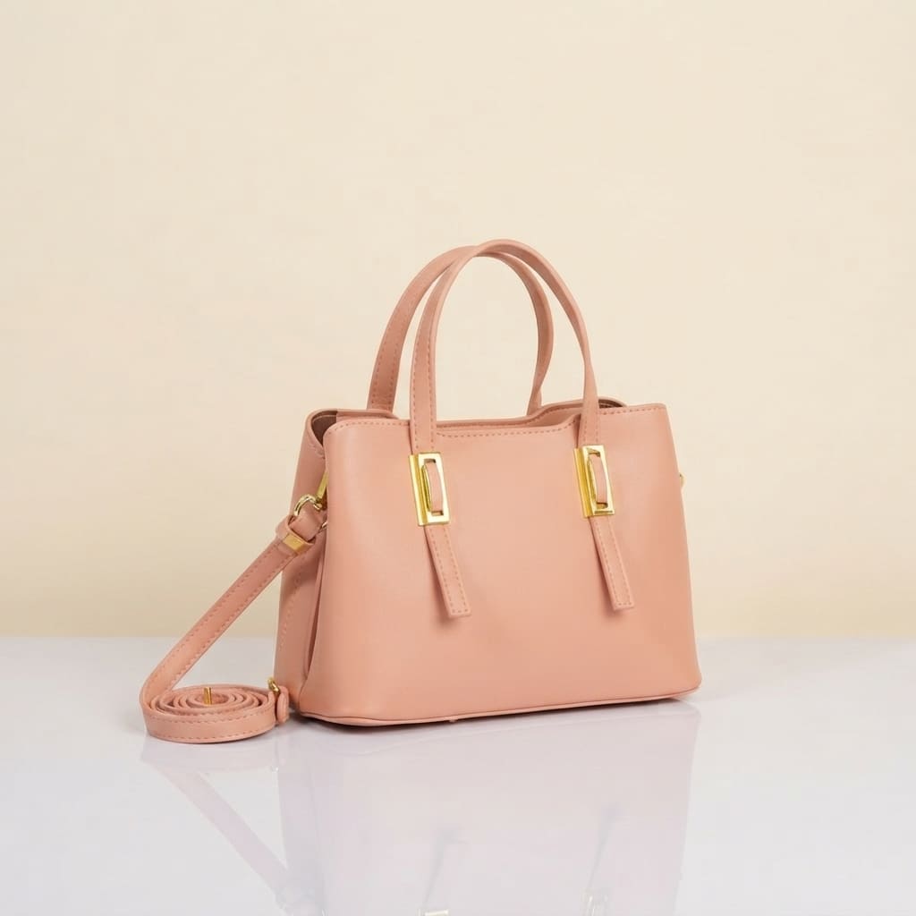 A light pink faux-leather handbag with dual top handles, a detachable shoulder strap, and gold-tone hardware, displayed on a reflective white surface against a beige background.