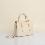 An white leather handbag with gold-tone hardware and a matching detachable shoulder strap, displayed on a light surface against a neutral cream background.