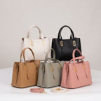 Five structured leather handbags in white, black, tan, gray, and blush pink are arranged on a white surface against a light gray studio background. Each bag has double top handles, a front zip closure, and gold-tone hardware. You can order these bags online from snapmart.