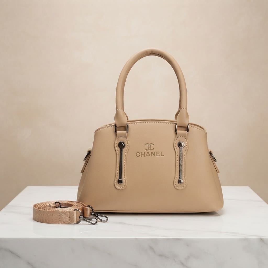 Beige faux leather handbag with branding, top handles, and a detachable strap on a white marble surface.