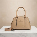 Beige faux leather handbag with branding, top handles, and a detachable strap on a white marble surface.