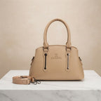 Beige faux leather handbag with branding, top handles, and a detachable strap on a white marble surface.