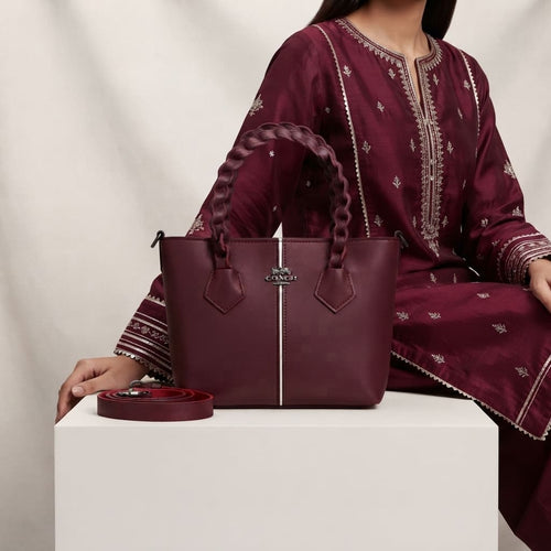 Model sitting next to the maroon crossbody handbag with a detachable red strap.