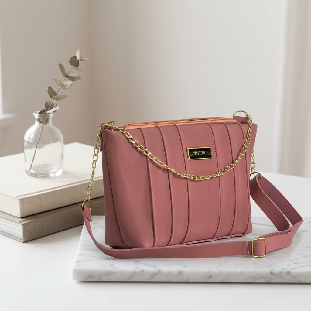 Dusty rose pleated shoulder bag with gold chain accent on marble slab next to books