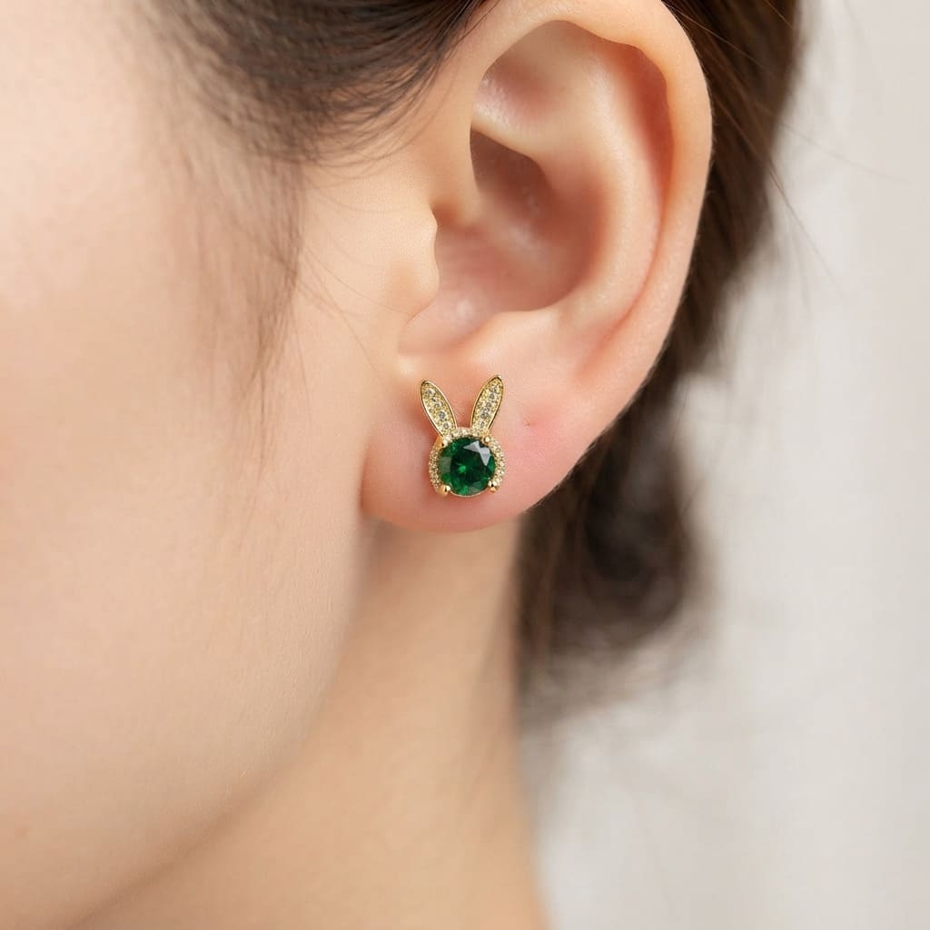 A pair of gold bunny stud earrings with green oval center stones wear by a women- Women Jewelry Pakistan