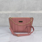 Dusty mauve faux leather crossbody bag featuring vertical stitching, a gold chain accent, and an adjustable strap on a marble surface.