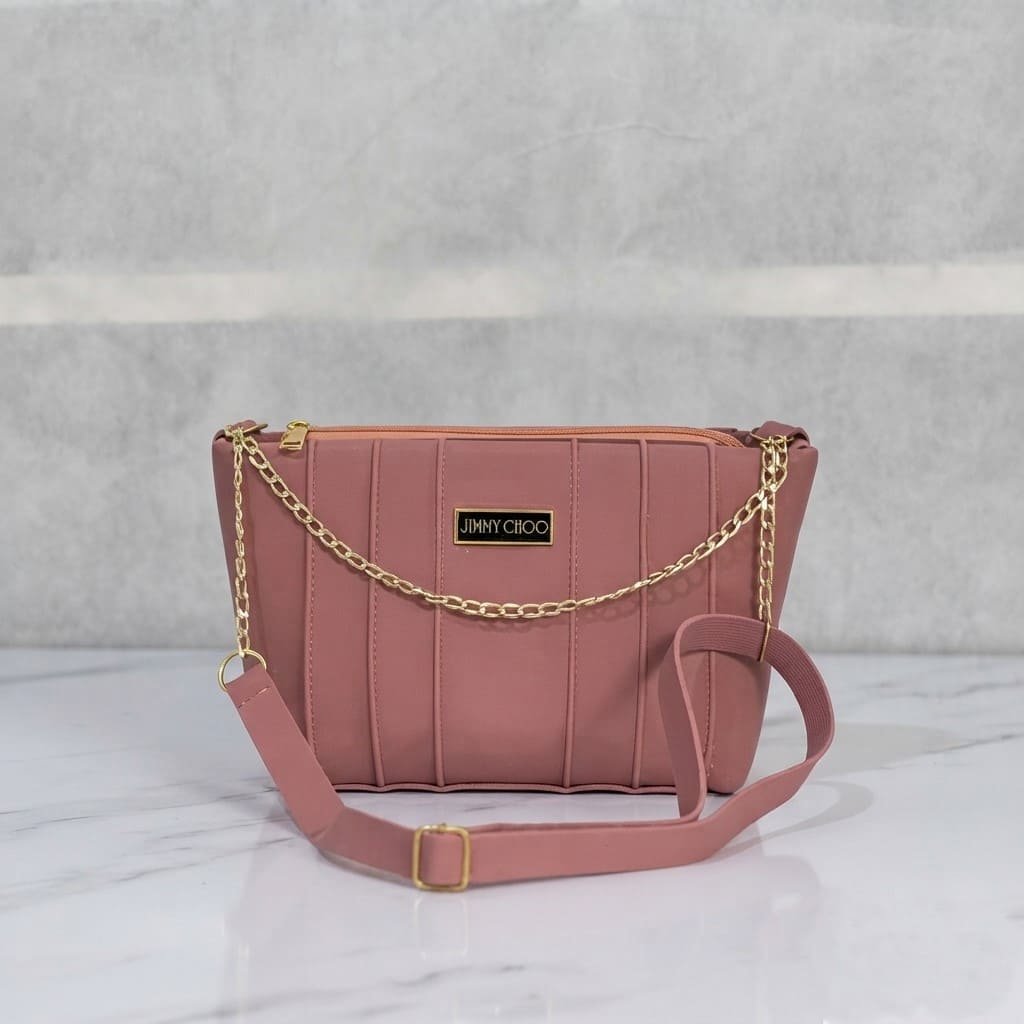 Dusty mauve faux leather crossbody bag featuring vertical stitching, a gold chain accent, and an adjustable strap on a marble surface.