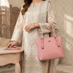 Woman standing next to a table holding the pink handbag with its shoulder strap placed nearby.