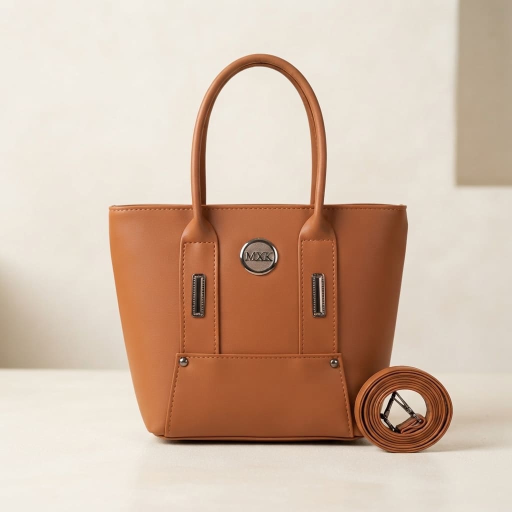 Tan faux leather handbag with metal logo, top handles, and a rolled shoulder strap on a table.
